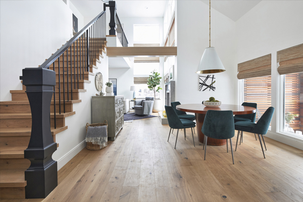 Modern open-concept living space featuring a wooden staircase, dining area with teal chairs, and large windows for natural light. In luxurious modern farmhouse built by Cortina Crafted Homes