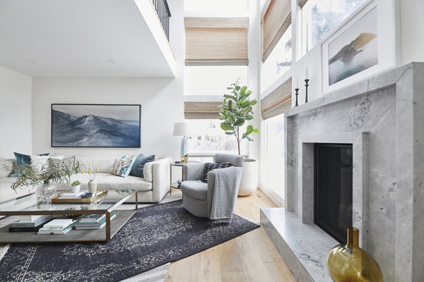 Modern open-concept living space featuring a wooden staircase, dining area with teal chairs, and large windows for natural light. In luxurious modern farmhouse built by Cortina Crafted Homes