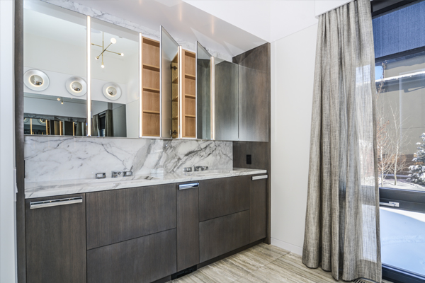 Modern bathroom vanity featuring marble countertop, sleek cabinetry, and a lighted mirror, with a large window dressed in elegant curtains.