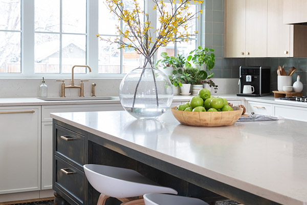 Bright kitchen with a large island, featuring white bar stools, and gold finishings. Natural light floods the space in custom home built by Cortina Crafted Homes in Calgary