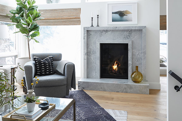 Cozy living room featuring a marble fireplace, modern furniture, with warm light from a fire and natural sunlight streaming. Built by Calgary custom home builder, Cortina.