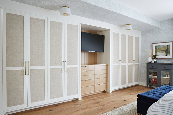 Stylish bedroom with white cabinets featuring linen panels, and a dark gray dresser on wooden flooring, in Calgary custom home built by Cortina