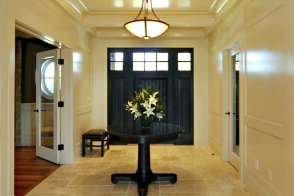Bright entryway featuring a round table with flowers, dark blue doors, and stylish lighting in a beige-toned decor.