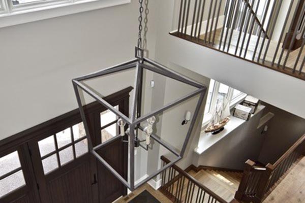 A geometric metal chandelier hangs from the ceiling of a stylish staircase, illuminating a bright, open foyer.