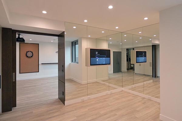 Bright and modern basement featuring mirrored walls, recessed lighting, a dartboard, and a wall-mounted TV display.